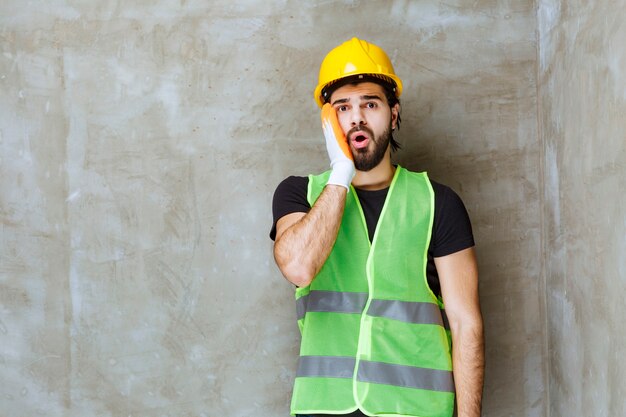 Ingenieur in gelber Maske und Industriehandschuhen sieht verwirrt und verängstigt aus