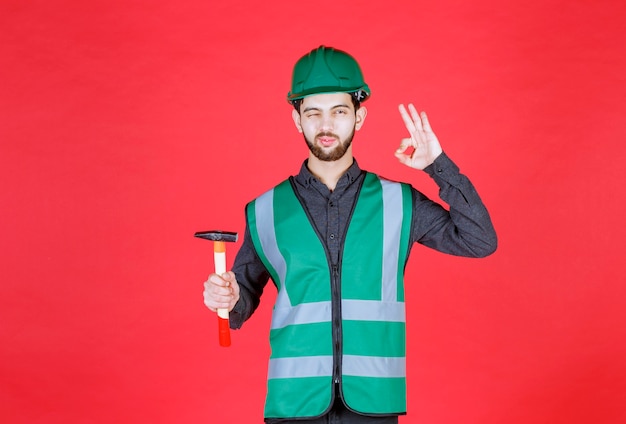 Ingenieur in grüner Uniform und Helm, der eine Holzaxt hält und ein positives Handzeichen zeigt.