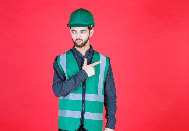 Ingenieur in grüner Uniform und Helm nach hinten zeigend.