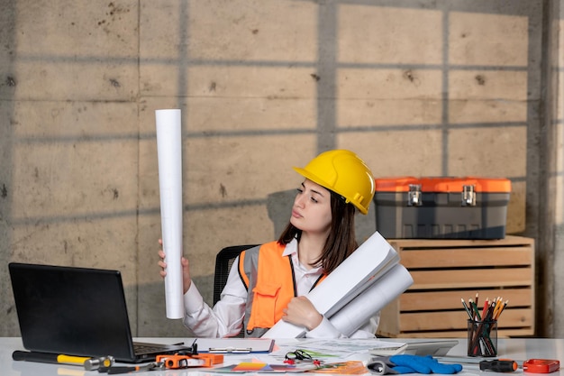 Ingenieur in Helm und Weste Bauarbeiterin intelligentes junges süßes brünettes Mädchen mit Papierrollen