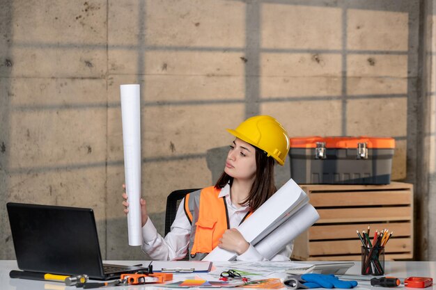 Ingenieur in Helm und Weste Bauarbeiterin intelligentes junges süßes brünettes Mädchen mit Papierrollen