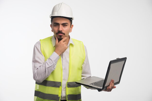 Ingenieur in Uniform hält einen Laptop und denkt nach.