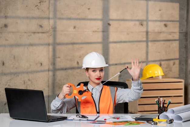 Ingenieur intelligente junge niedliche blonde Mädchen Zivilarbeiterin in Helm und Weste, die zu Hause arbeitet