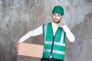 Kostenloses Foto ingenieur mann in gelber uniform und helm hält ein papppaket und bittet um einen anruf.