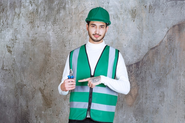 Ingenieur Mann in gelber Uniform und Helm mit blauen Zangen zur Reparatur.