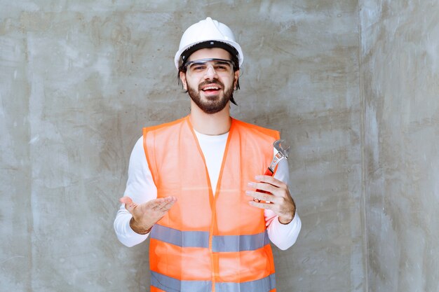 Ingenieur Mann in weißem Helm und Schutzbrille mit Metallschlüsseln.