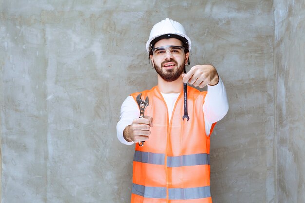 Ingenieur Mann in weißem Helm und Schutzbrille mit Metallschlüsseln.