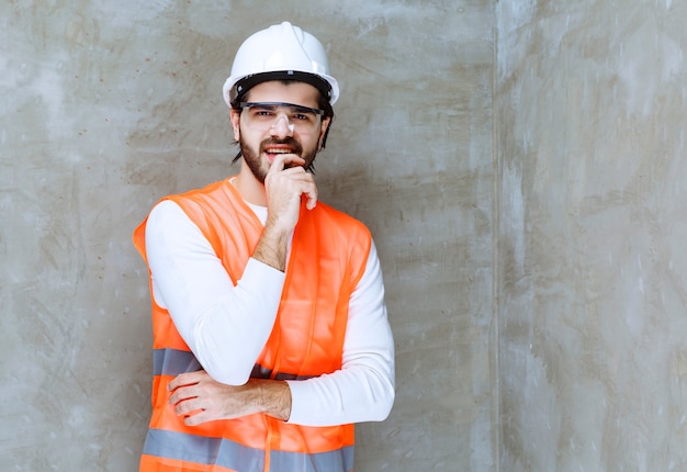 Ingenieur Mann in weißem Helm und Schutzbrille sieht verwirrt und nachdenklich aus.