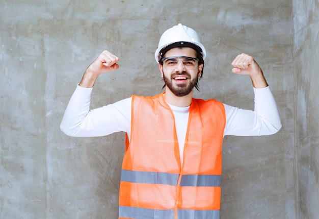 Ingenieur Mann mit weißem Helm und Schutzbrille, die seine Armmuskulatur zeigt.