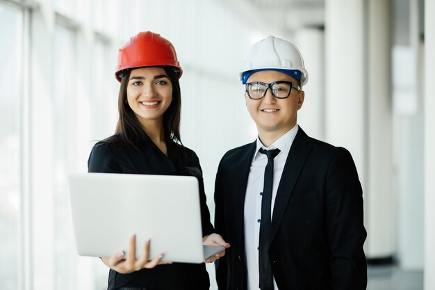 Ingenieur- und Architekturkonzept. Ingenieure, die auf einer Baustelle arbeiten, die Laptop hält, Architektenmann, der mit Inspektion der Ingenieurin am Arbeitsplatz für Architekturplan arbeitet