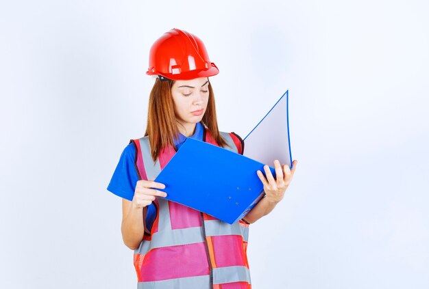 Ingenieurfrau im roten Helm, der einen blauen Projektordner hält.