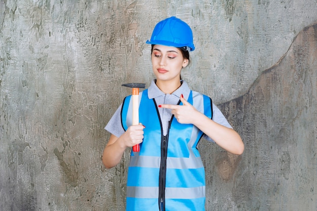 Ingenieurin in blauer ausrüstung und helm, die eine axt mit holzgriff hält.