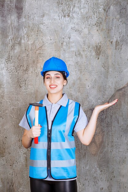 Ingenieurin in blauer Ausrüstung und Helm, die eine Axt mit Holzgriff hält.