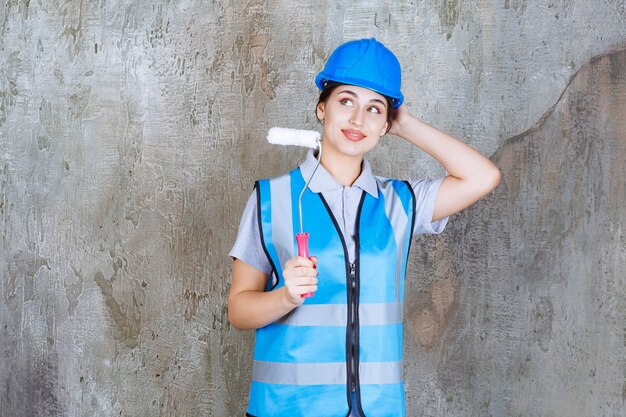 Ingenieurin in blauer Uniform und Helm hält eine Trimmrolle zum Malen und Denken und Planen.