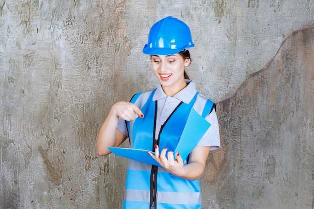 Ingenieurin in blauer Uniform und Helm mit einem blauen Berichtsordner.