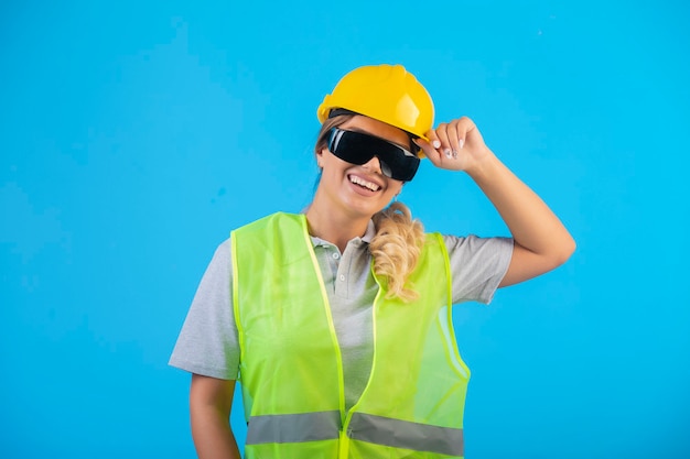Ingenieurin in gelbem Helm und Ausrüstung, die eine strahlverhindernde Brille trägt und sich positiv fühlt.