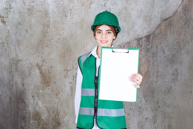 Ingenieurin in grüner Uniform und Helm, die die Projektliste demonstriert