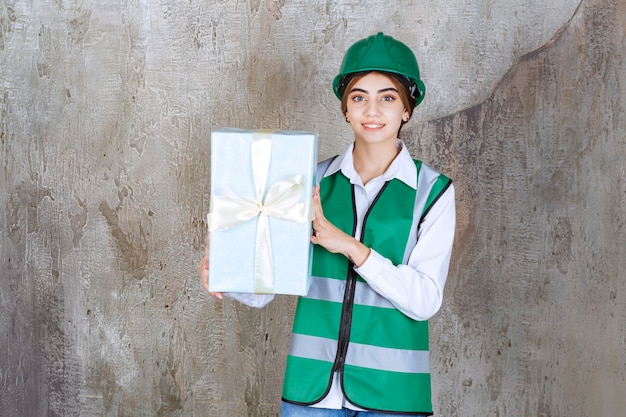 Ingenieurin in grüner Uniform und Helm mit einer blauen Geschenkbox.