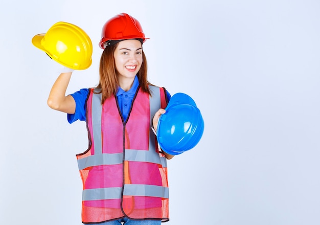 Ingenieurmädchen in Uniform, das blaue und gelbe Helme hält und eine Wahl trifft.