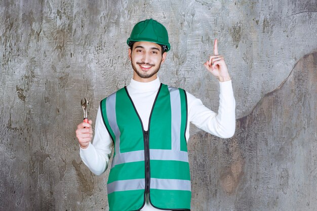 Ingenieursmann in gelber Uniform und Helm, der einen Metallschlüssel zur Reparatur hält und nachdenklich aussieht