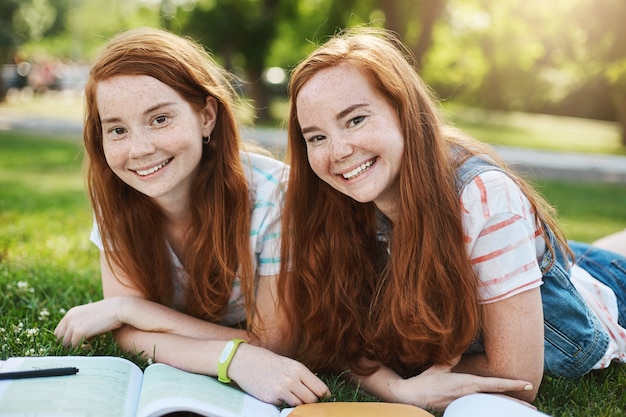 Kostenloses Foto ingwer-zwillingsmädchen verbringen ihre sommerferien, um sich auf die universitätsprüfungen vorzubereiten. zukünftiger arzt und anwalt, die spaß haben, an einem sonnigen tag im park lächelnd zu haben.