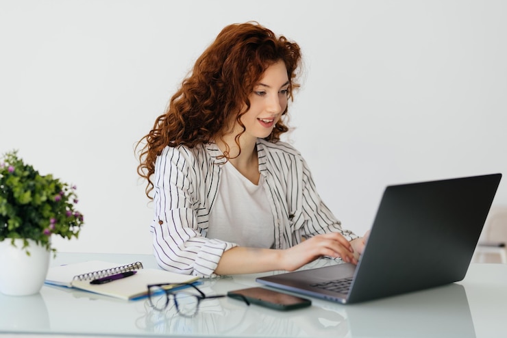 Kostenlose Foto ingwerfrau tippt auf laptop, während sie zu hause am schreibtisch sitzt