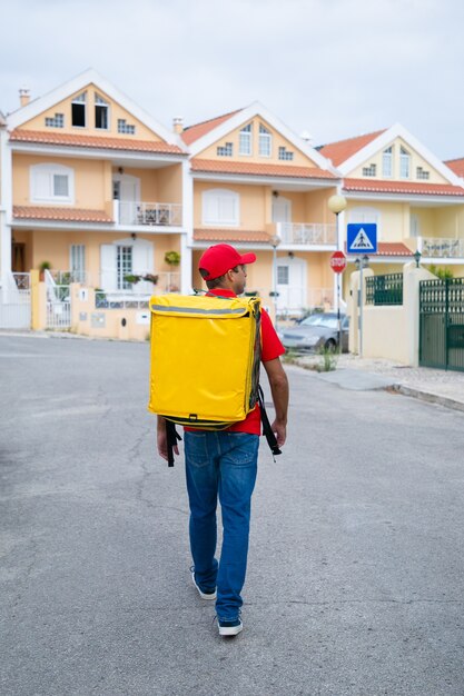 Inhaltslieferant, der gelben Wärmebeutel trägt. Kurier mittleren Alters im roten Hemd auf der Suche nach Adresse und Lieferauftrag.