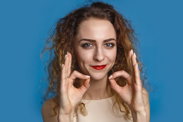 Innenaufnahme der friedlichen glücklichen jungen Frau mit dem lockigen Haar, das sich entspannt fühlt, Yoga-Meditation praktizierend, lächelnd. Rücksichtnahme, Ruhe, ruhige Atmosphäre, Entspannung und Ausgeglichenheit