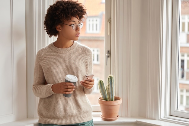 Innenaufnahme der nachdenklichen dunkelhäutigen Frau verwendet Smartphone für Online-Kommunikation