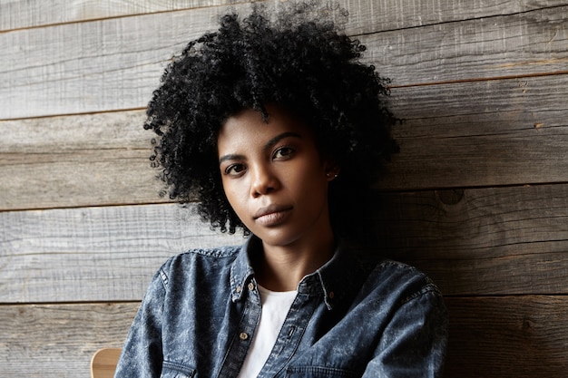 Innenaufnahme der stilvollen jungen afroamerikanischen Frau mit dem lockigen Haar, das trendige Jeanskleidung trägt