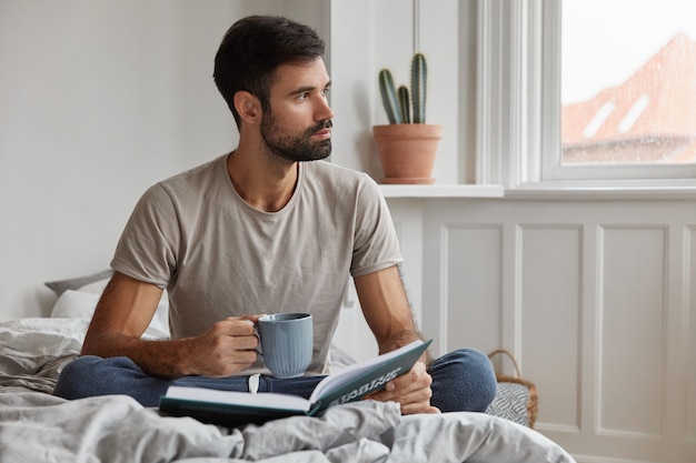 Innenaufnahme des attraktiven bärtigen Kerls, der zu Hause während der Arbeit aufwirft