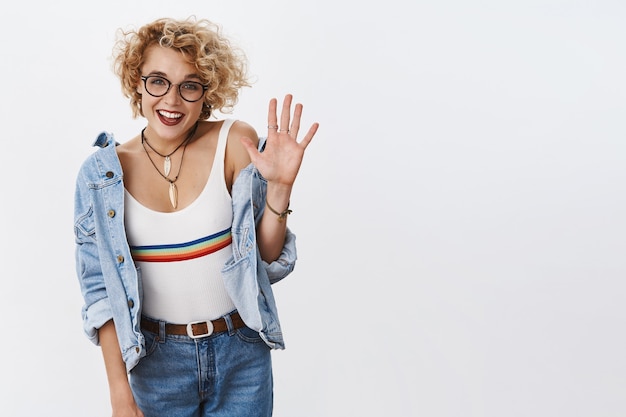 Kostenloses Foto innenaufnahme einer enthusiastischen, stilvollen weiblichen blondine mit brille und durchbohrter nase, die die handfläche anhebt und breit lächelt und empfehlungen und positive meinungen zur werbung gibt