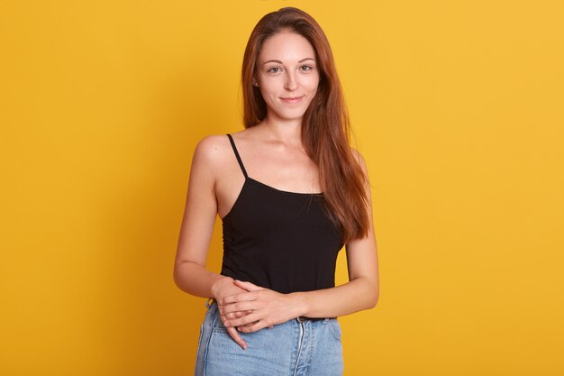 Innenfoto der lebhaften Frau, die Jeans und schwarzes T-Shirt trägt, das auf Kamera mit angenehmem Lächeln und aufwirft. Kopieren Sie Platz für Werbung.