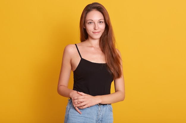 Innenfoto der lebhaften Frau, die Jeans und schwarzes T-Shirt trägt, das auf Kamera mit angenehmem Lächeln und aufwirft. Kopieren Sie Platz für Werbung.