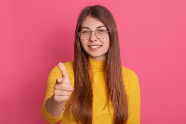 Innenporträt der angenehmen fröhlichen jungen Dame, die isoliert über rosa Wand im Studio aufwirft, aufrichtig lächelt, Geste macht, in Hochstimmung ist, Zeit allein verbringt. Emotionskonzept.