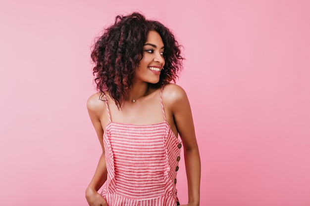 Innenporträt des glücklichen attraktiven Mädchens mit schneeweißem Lächeln. Frau im rosa Sommerkleid, das für Fotoshooting aufwirft.