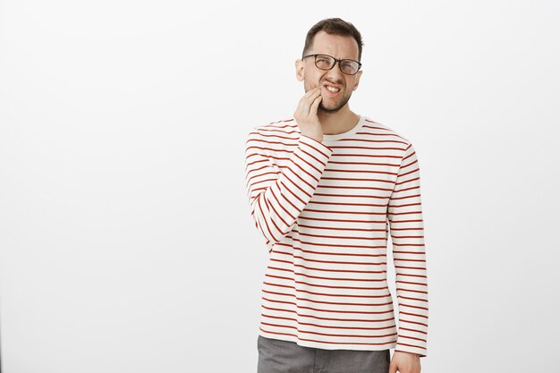 Innenporträt eines unzufriedenen unbequemen europäischen Mannes in Brille, der unter Zahnschmerzen leidet
