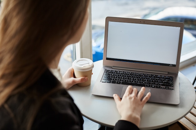 Innenrückansicht der stilvollen Frau, die im Café sitzt, Tasse Kaffee trinkt und mit Laptop arbeitet