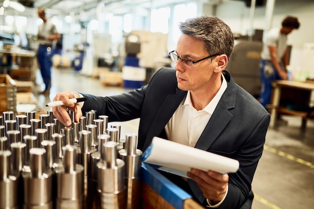 Inspektor für Qualitätskontrolle, der hergestellte Stahlzylinder in einer Fabrik untersucht