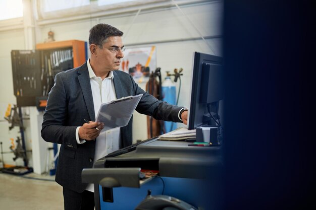 Inspektor im mittleren Erwachsenenalter analysiert Daten, während er den Computer in der Autowerkstatt verwendet