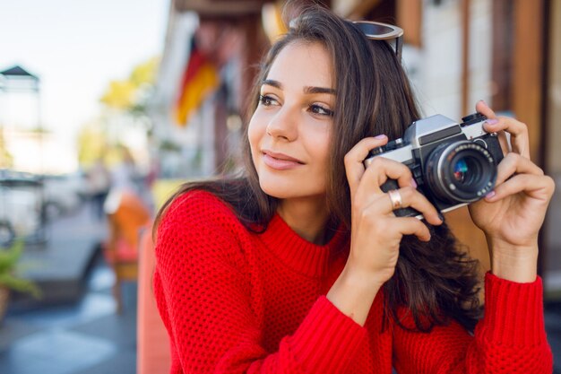 Inspirierte brünette Frau, die Spaß hat und Fotos in ihren Ferien macht. Kalte Jahreszeit. Trägt einen stylischen roten Strickpullover.