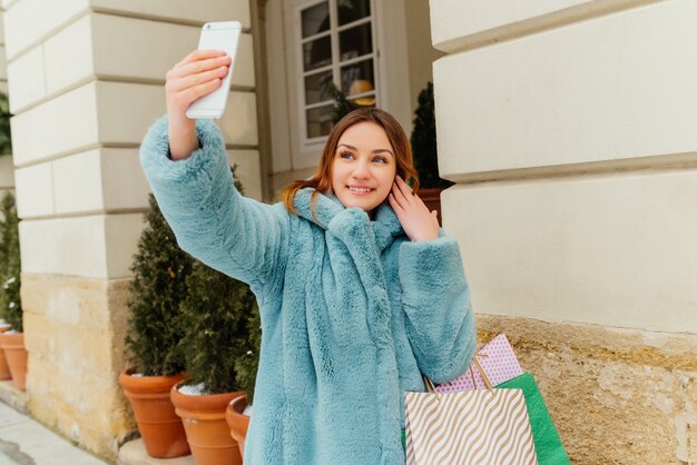 Inspiriertes braunhaariges Mädchen, das selfie nach dem Einkauf und dem Lachen macht.