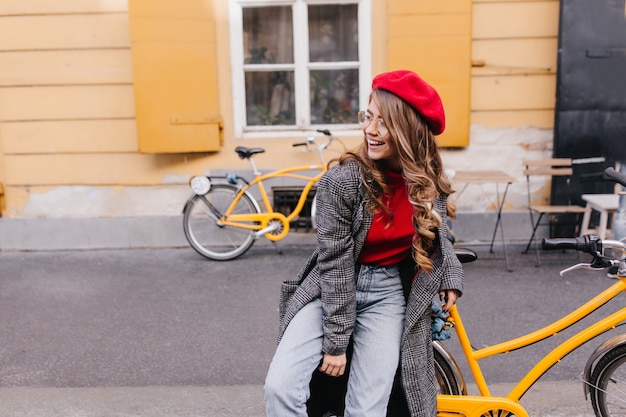 Inspiriertes Mädchen in Blue Jeans posiert auf der Straße und schaut sich mit aufrichtigem Lachen um