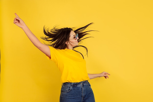 Inspiriertes Tanzen mit Sonnenbrille. Kaukasische Frau auf gelber Wand. Schönes weibliches brünettes Modell im lässigen Stil. Konzept der menschlichen Emotionen, Gesichtsausdruck, Verkauf, Anzeige, Copyspace.