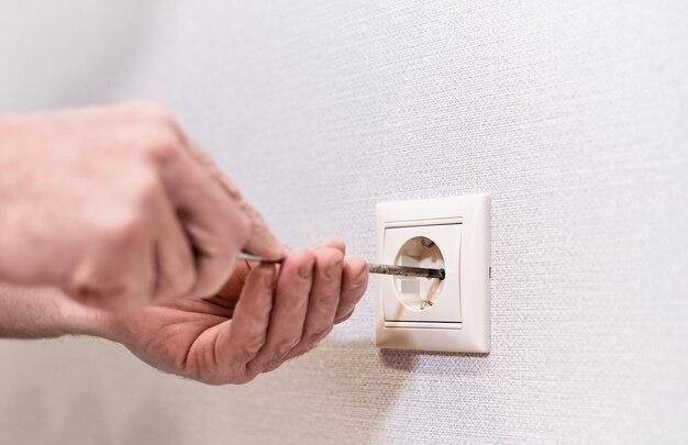 Installation von Steckdosen in einer neuen Wohnung Nahaufnahme der Hände eines kaukasischen Elektrikers, der einen Schraubendreher hält, der an der elektrischen Steckdose des elektrischen Wohnsystems arbeitet