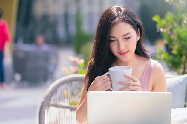 Intelligente, attraktive asiatische Frau, lässiges Tuch im Freien, entspannen Sie sich beim Arbeiten mit Laptop und Smartphone im urbanen Lebensstil des Café-Restaurants