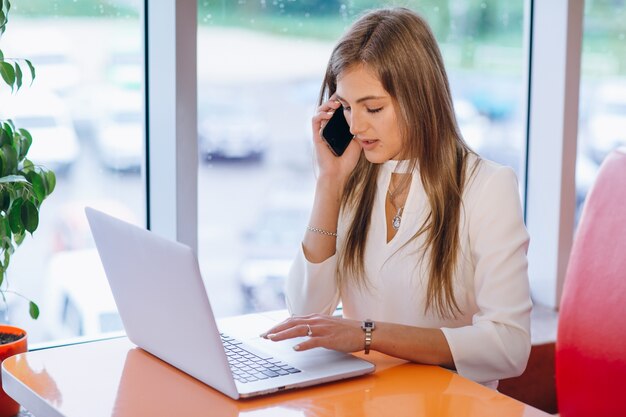 Intelligente Frau auf ihrem Laptop eingeben, während Sie einen Anruf annehmen