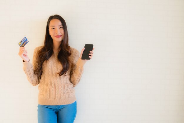 Intelligentes Mobiltelefon des schönen jungen asiatischen Gebrauches des Porträts mit Kreditkarte