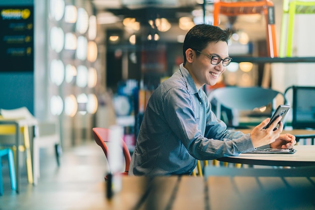 Intelligentes Vertrauen asiatischer Startup-Unternehmer Geschäftsinhaber Geschäftsmann Lächeln Hand verwenden Smartphone woking im Bürohintergrund