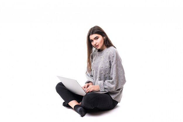 Interessierte Brünette Mädchen Modell in grauem Pullover sitzen auf dem Boden und arbeiten studie auf ihrem Laptop